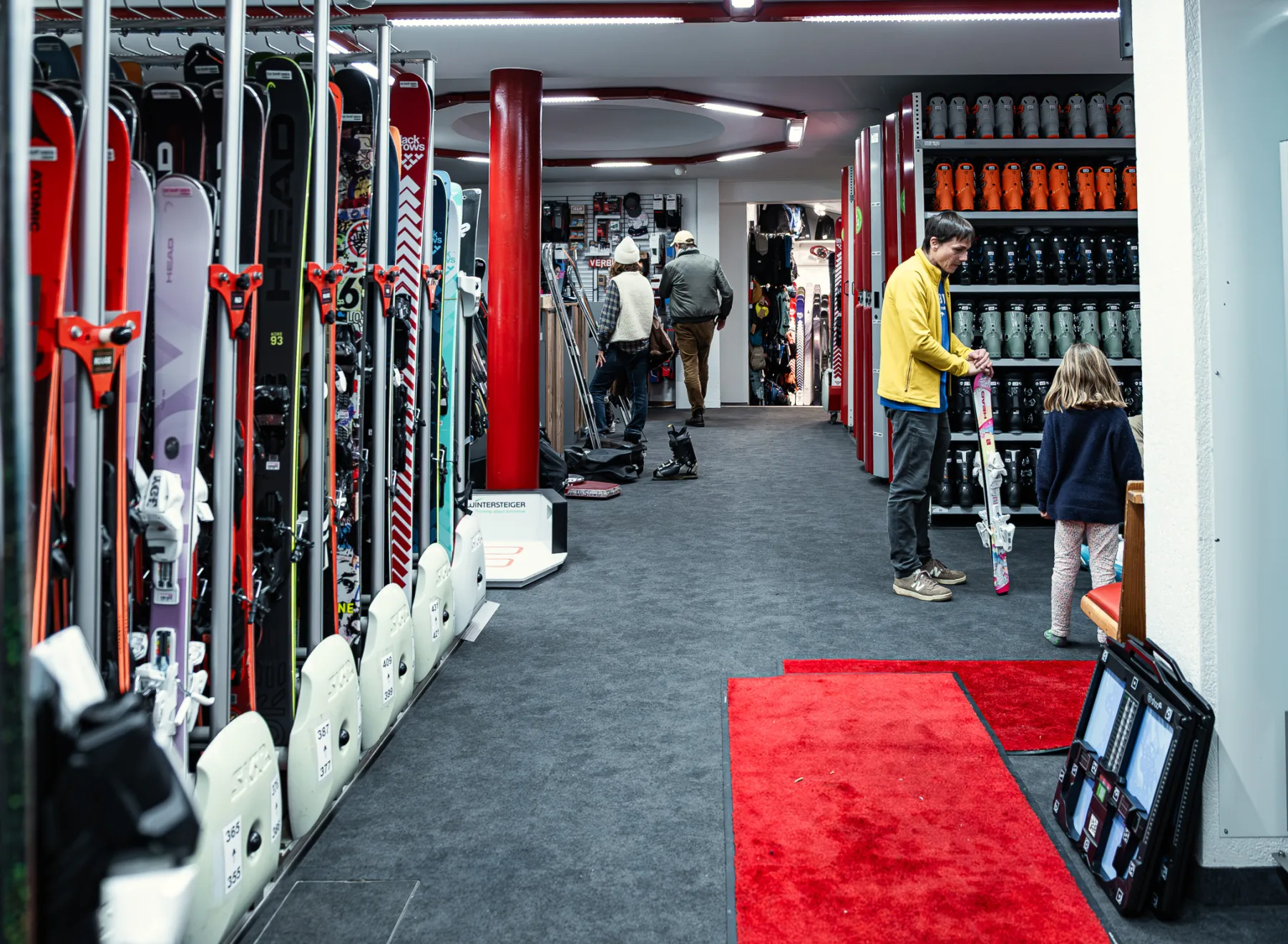L'allée du parc de location, skis sur les racks et clients au comptoir.